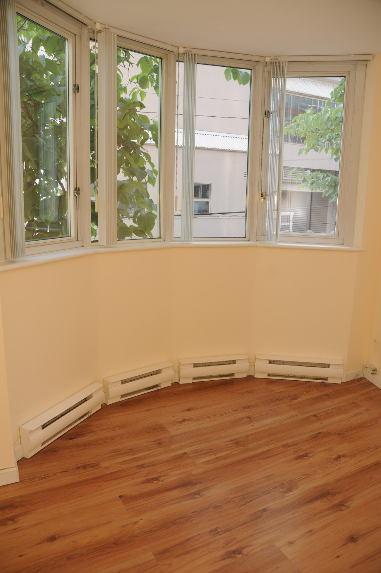 Bright living room with hardwood floors and bay windows, offering a city view. - 211 - 1166 Melville St, Vancouver Downtown