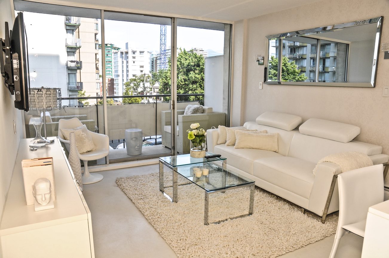 Bright living room with white furniture, city view, and large windows. - 302 - 1251 Cardero, Vancouver Downtown