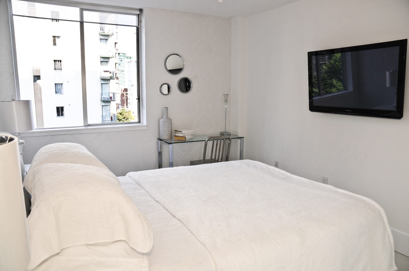 Bright bedroom with city view and modern decor, featuring a flat-screen TV and a glass nightstand. - 302 - 1251 Cardero, Vancouver Downtown