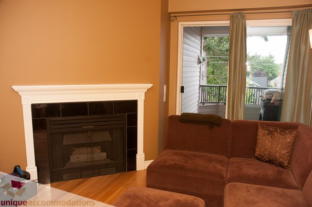 Furnished living room with brown couches and fireplace, hardwood floors, and sliding glass door leading to balcony.