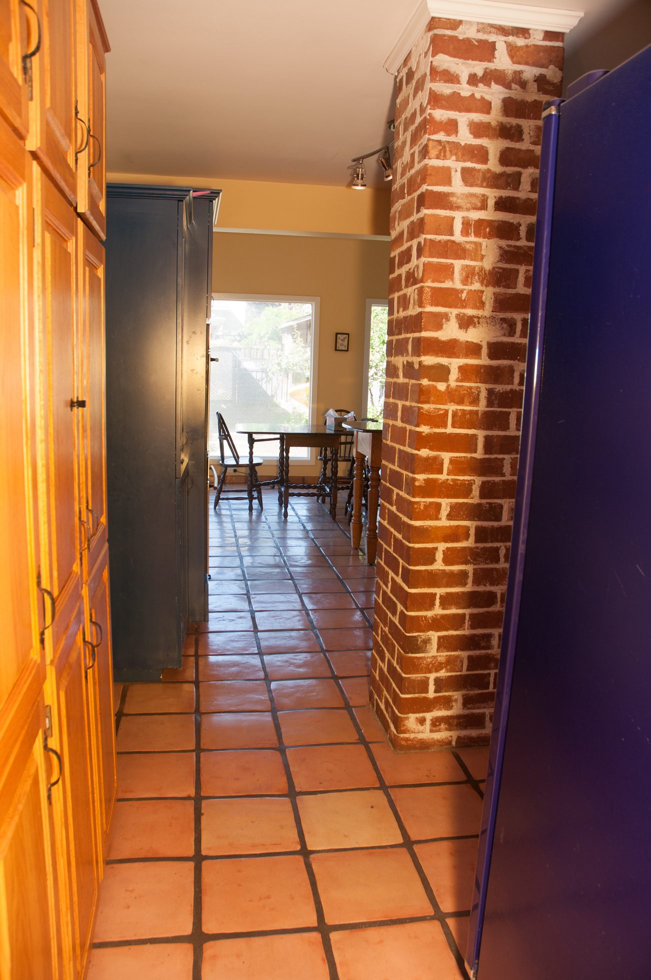 Bright kitchen with terracotta tile floors and brick pillar, leading to a dining area with wooden furniture and large...