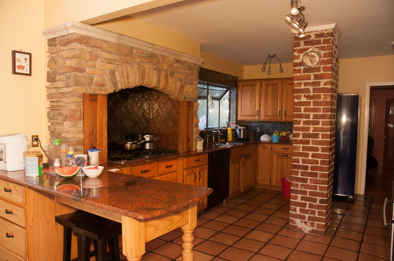 Bright kitchen with stone fireplace and wooden cabinets, featuring a granite countertop and tiled floor. - 3249 West 36th Ave, Vancouver West Side