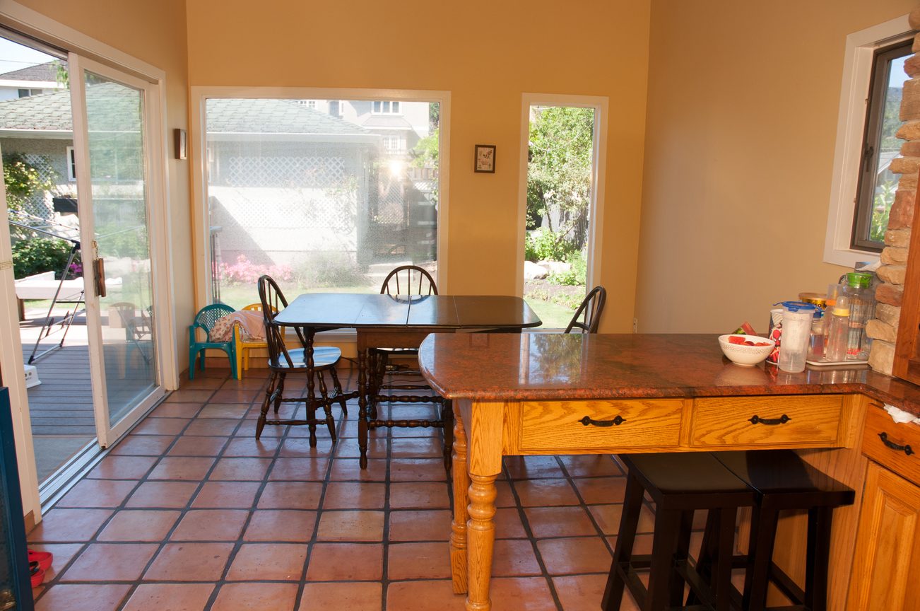 Bright dining area with wooden tables and terracotta tile flooring, leading to a sunny backyard view. - 3249 West 36th Ave, Vancouver West Side
