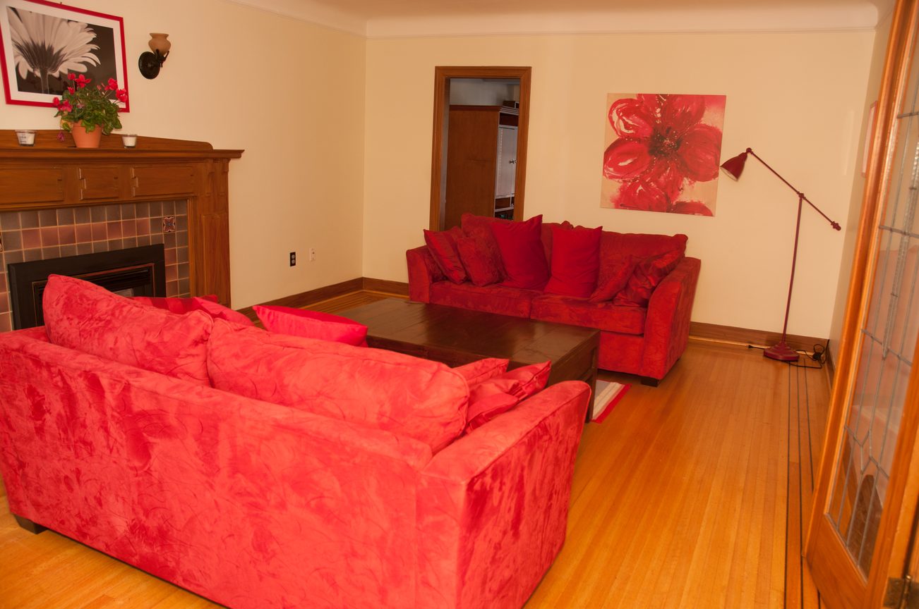 Furnished living room with red sofas, hardwood floors, and a fireplace. - 3249 West 36th Ave, Vancouver West Side