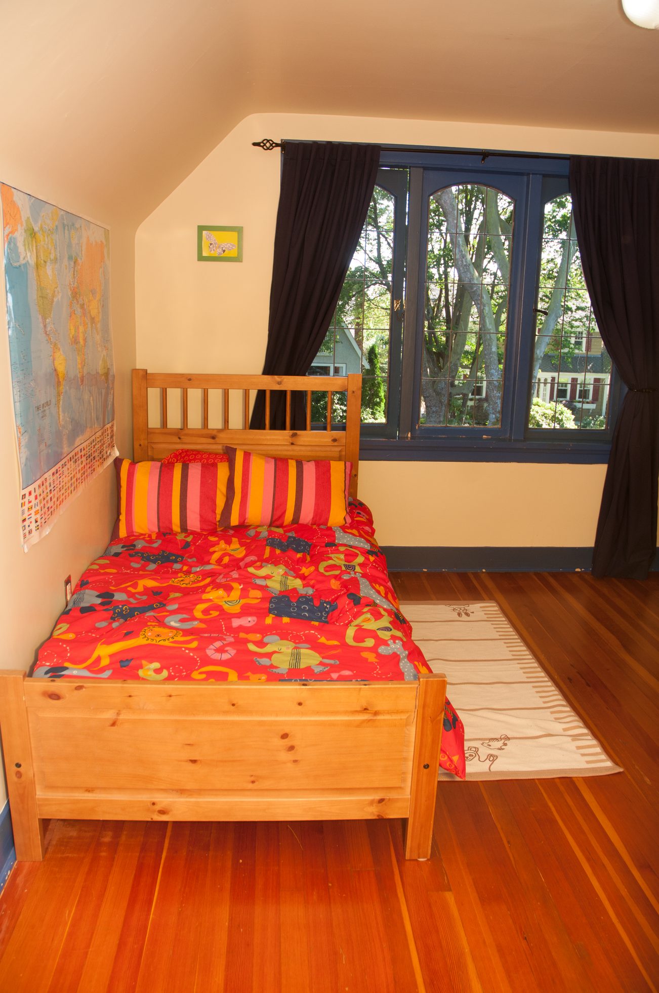 Bright bedroom with hardwood floors, colorful bedding, and a large window with a view of trees. - 3249 West 36th Ave, Vancouver West Side