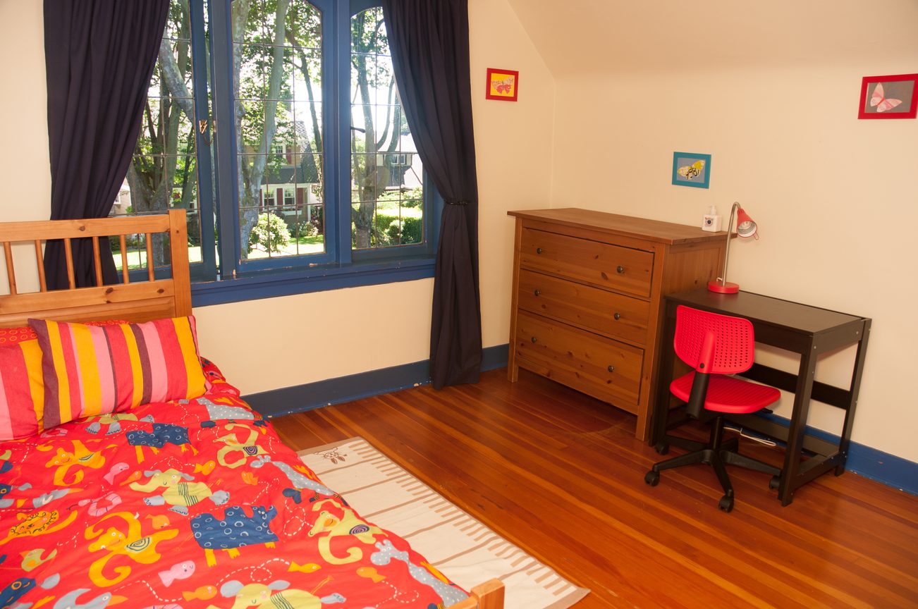 Bright bedroom with hardwood floors, colorful bedding, and a desk with red chair. - 3249 West 36th Ave, Vancouver West Side