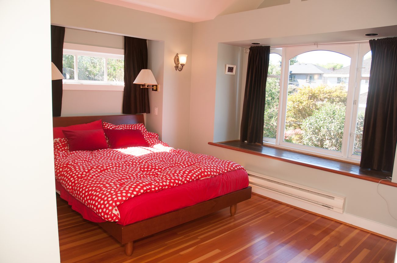 Furnished bedroom with red polka dot bedding and hardwood floors, city view through large windows. - 3249 West 36th Ave, Vancouver West Side