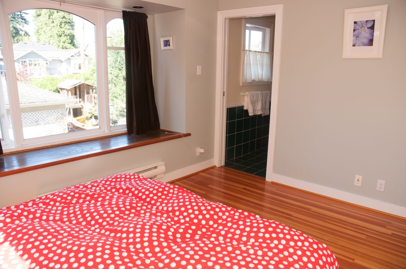 Bright bedroom with hardwood floors, red polka-dot bedding, and a large window with a city view. - 3249 West 36th Ave, Vancouver West Side