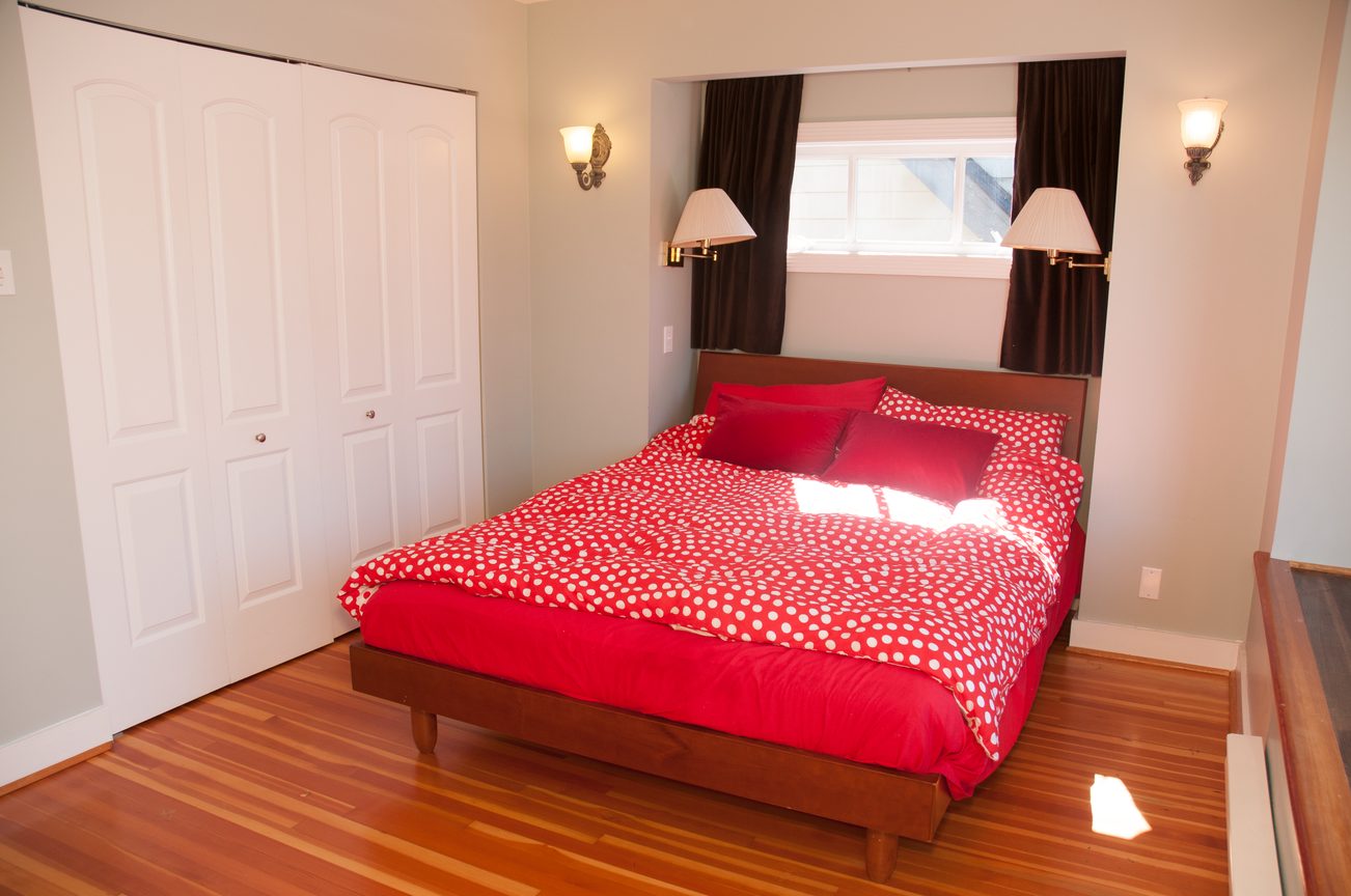Furnished bedroom with red polka dot bedding, hardwood floors, and wall sconces. - 3249 West 36th Ave, Vancouver West Side