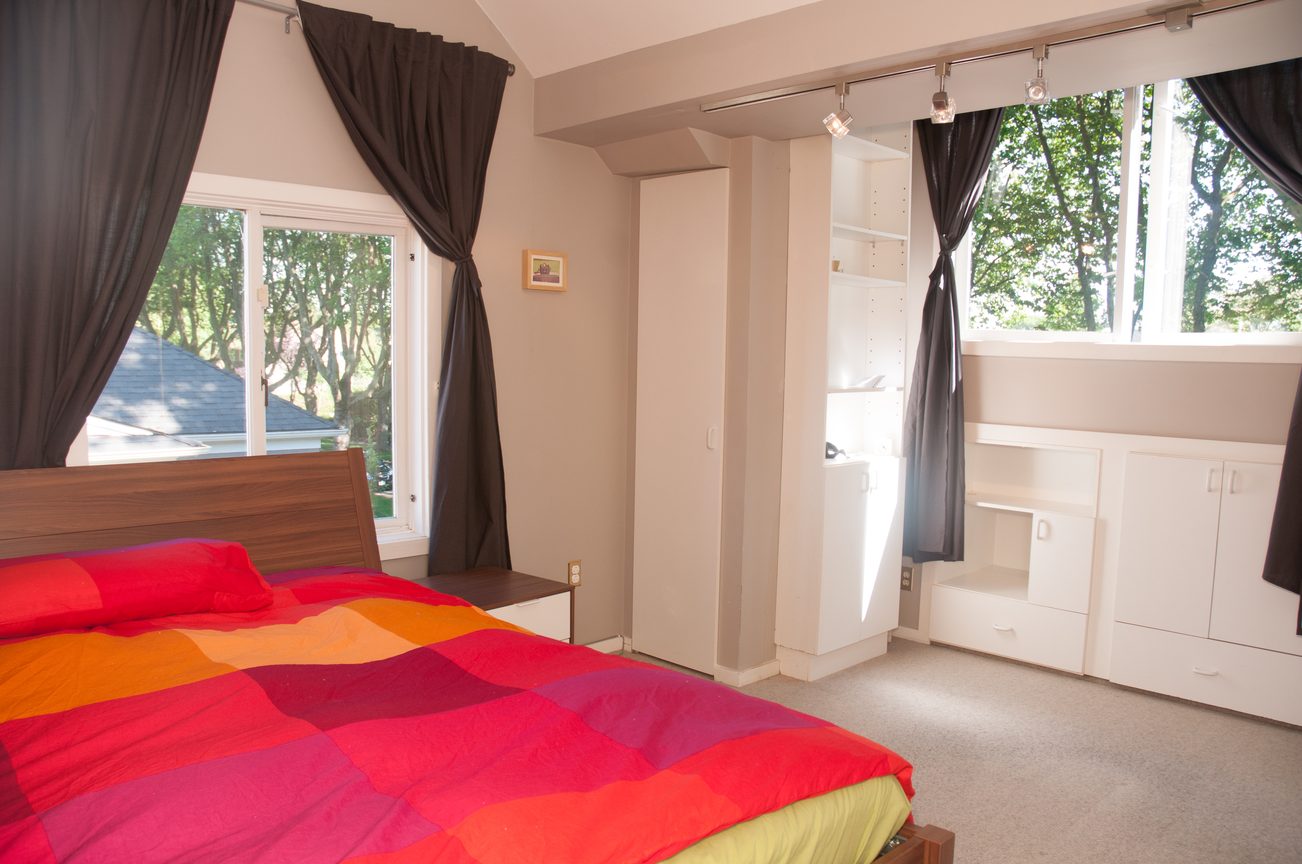 Bright bedroom with colorful bedding and large windows, offering a view of greenery. - 3249 West 36th Ave, Vancouver West Side