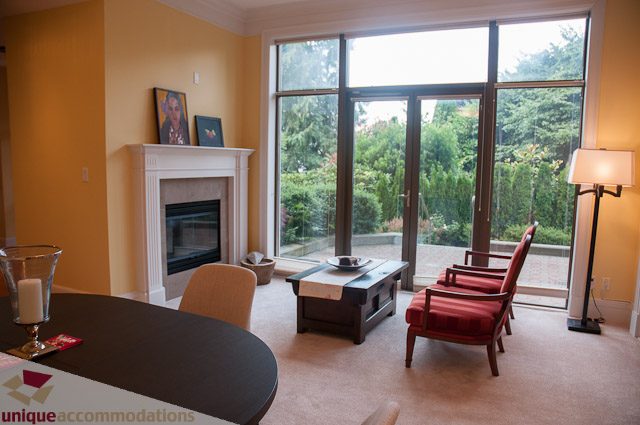 Spacious living room with large windows, fireplace, and outdoor view. - 103-2288 Bellevue Ave, West Vancouver