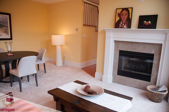 Furnished living room with fireplace and dining area, light yellow walls. - 103-2288 Bellevue Ave, West Vancouver