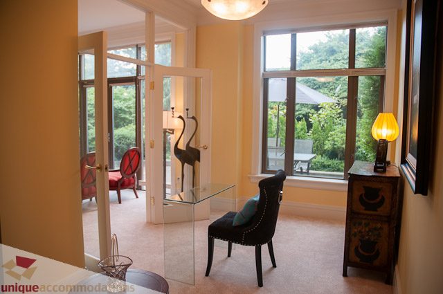 Bright living room with large windows and a view of greenery, featuring a glass-topped coffee table and a red armchair.