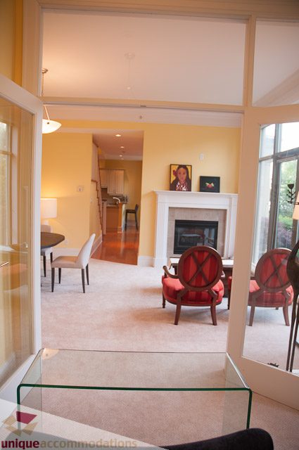 Furnished living room with fireplace, glass coffee table, and dining area visible in the background. - 103-2288 Bellevue Ave, West Vancouver