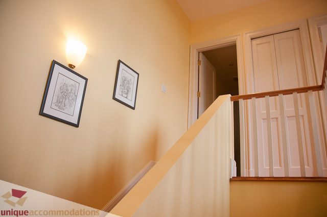 Staircase leading to upper level with framed artwork and warm lighting. - 103-2288 Bellevue Ave, West Vancouver