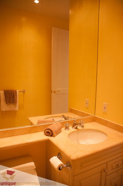 Furnished bathroom with yellow walls, double sink, and large mirror. - 103-2288 Bellevue Ave, West Vancouver