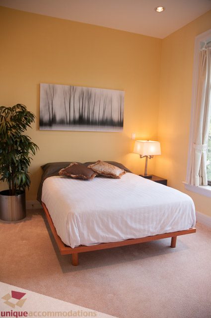 Spacious bedroom with a modern bed, warm lighting, and a large artwork on the wall. - 103-2288 Bellevue Ave, West Vancouver