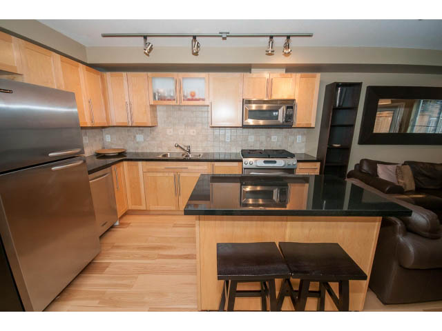 Bright kitchen with stainless steel appliances, hardwood floors, and a city view. - 204 - 122 East 3rd Street, North Vancouver
