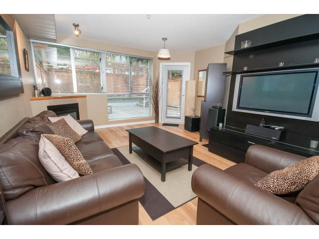 Furnished living room with brown leather furniture, hardwood floors, and a flat-screen TV mounted on a black wall.