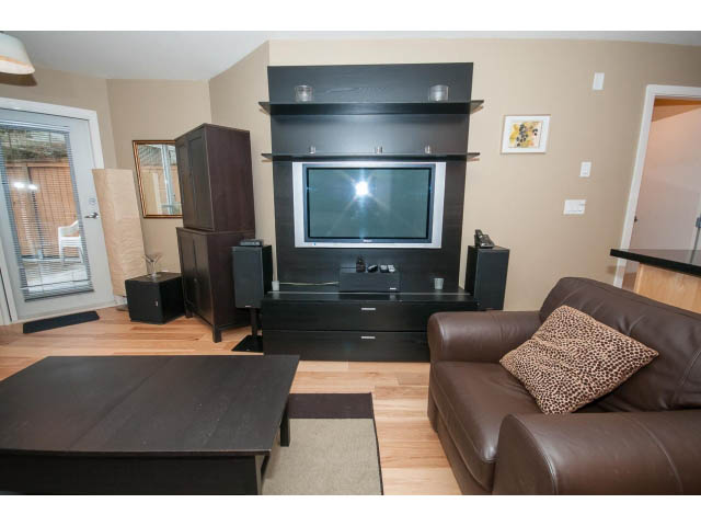 Furnished living room with hardwood floors, dark wood furniture, and a flat-screen TV mounted on a wall unit.