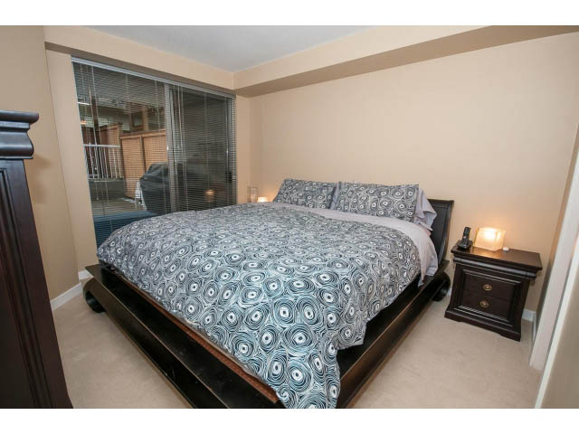 Furnished 1-bedroom + den with patterned bedding and sliding glass door leading to balcony. - 204 - 122 East 3rd Street, North Vancouver