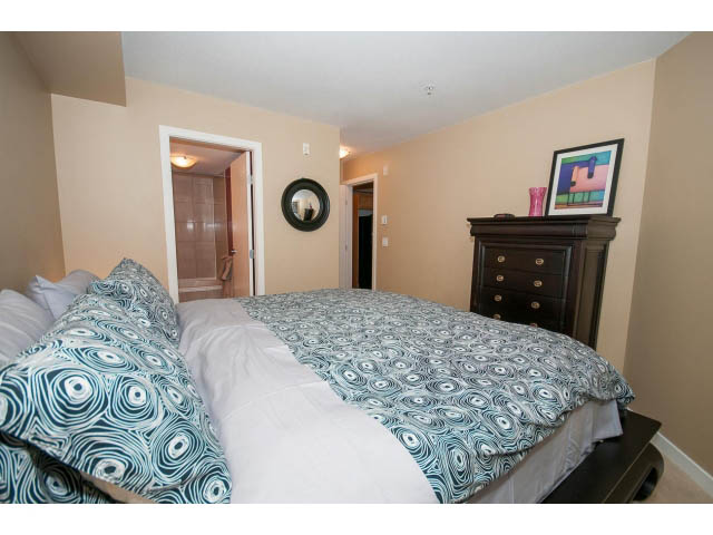 Furnished 1-bedroom + den with peacock-patterned bedding and a dark wood dresser. - 204 - 122 East 3rd Street, North Vancouver