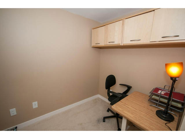 Furnished den with wooden desk, lamp, and storage cabinets. - 204 - 122 East 3rd Street, North Vancouver