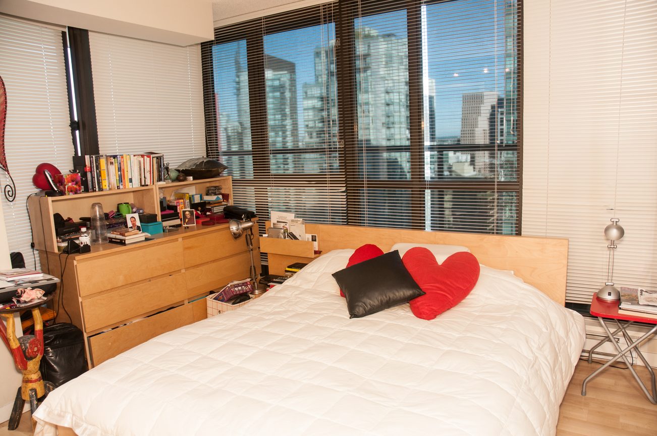 Bright bedroom with city view and wooden furniture, featuring a double bed with white bedding and red heart-shaped pillows.