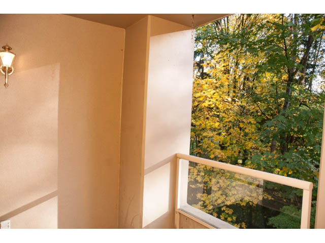 Bright living room with large window showing autumn foliage, light-colored walls, and wooden railings. - 308 - 1327 East Keith Road, North Vancouver