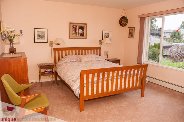 Spacious bedroom with wooden furniture, large window, and floral bedding. - 4559 W. 3rd Ave, Vancouver West Side