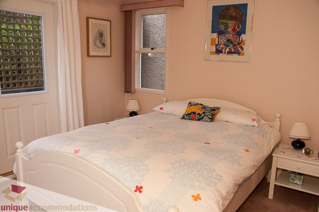 Bright bedroom with white bedding and colorful pillows, natural light from windows. - 4559 W. 3rd Ave, Vancouver West Side