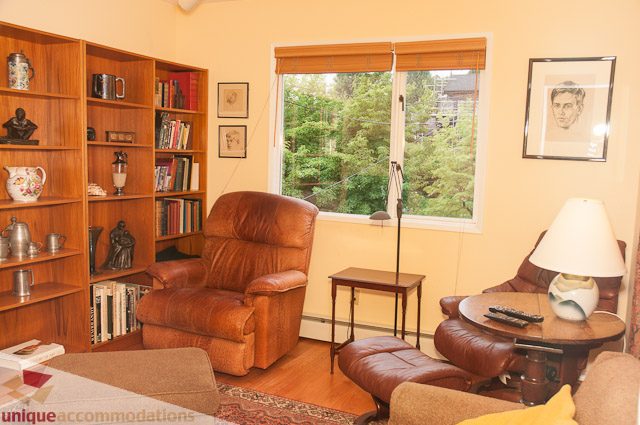 Furnished living room with leather furniture, bookshelves, and a large window view of greenery. - 4559 W. 3rd Ave, Vancouver West Side
