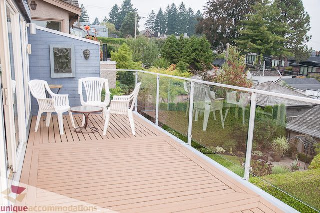 Furnished balcony with white chairs and glass railing, overlooking greenery and rooftops. - 4559 W. 3rd Ave, Vancouver West Side
