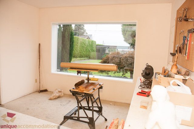 Bright living room with large window, tools on wall, cluttered workspace. - 4559 W. 3rd Ave, Vancouver West Side