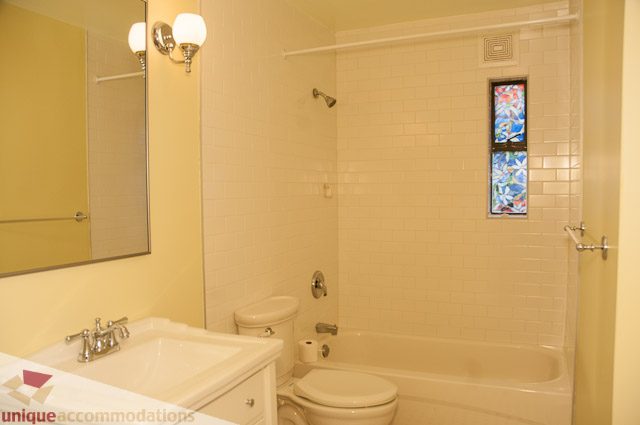 Bright bathroom with white tile, stained glass window, and dual sinks. - 3 - 1786 Esquimalt Avenue, West Vancouver