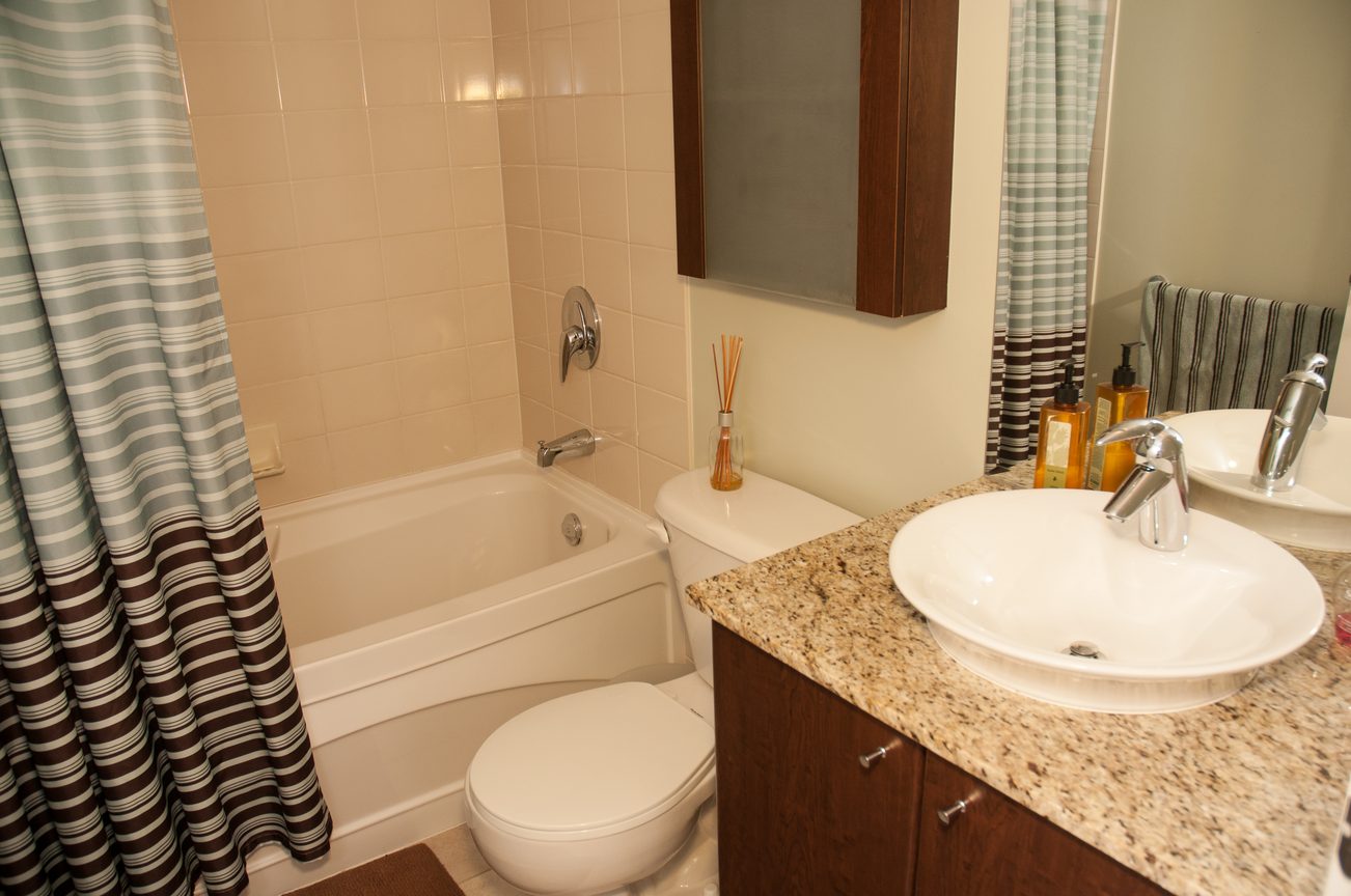 Bathroom with granite countertops, modern fixtures, and a striped shower curtain. - 1601-1199 Seymour Street, Vancouver Downtown