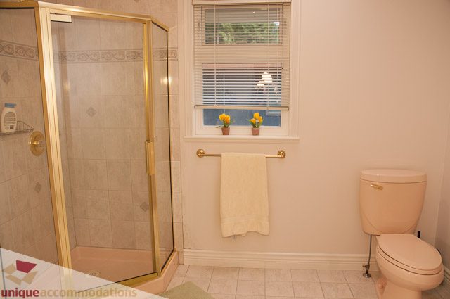 Bright bathroom with beige tiles, gold-framed shower, and window with yellow flowers. - 1115 Prospect Ave, North Vancouver