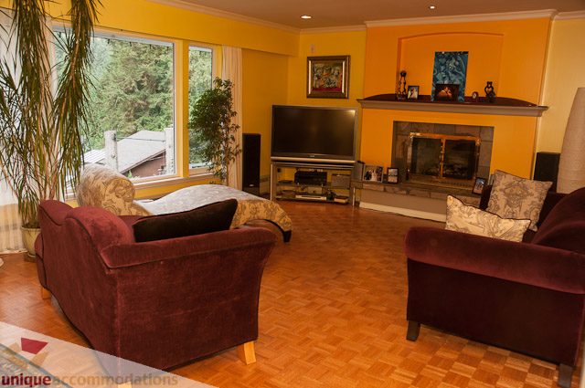 Furnished living room with hardwood floors, fireplace, and large windows. - 1650 Riverside Drive, North Vancouver