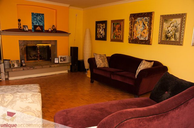 Furnished living room with vibrant yellow walls, modern artwork, and a cozy fireplace. - 1650 Riverside Drive, North Vancouver