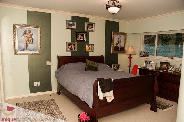 Furnished bedroom with green accent wall, framed artwork, and wooden furniture. - 1650 Riverside Drive, North Vancouver