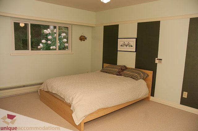 Bright bedroom with wooden beds, green accent wall, and floral window view. - 1650 Riverside Drive, North Vancouver