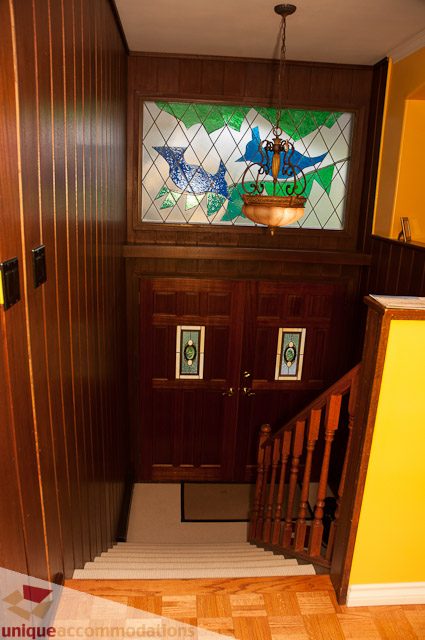 Staircase leading to a 3-bedroom suite with wooden paneling and a stained glass window above the door. - 1650 Riverside Drive, North Vancouver