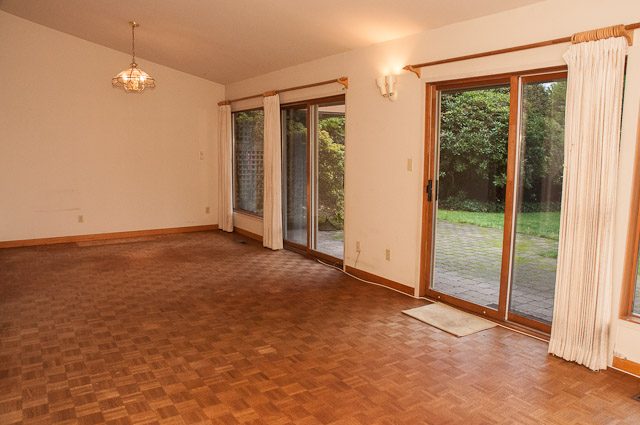 Empty living room with hardwood floors and sliding glass doors leading to a garden. - 2919 Mathers Ave, West Vancouver