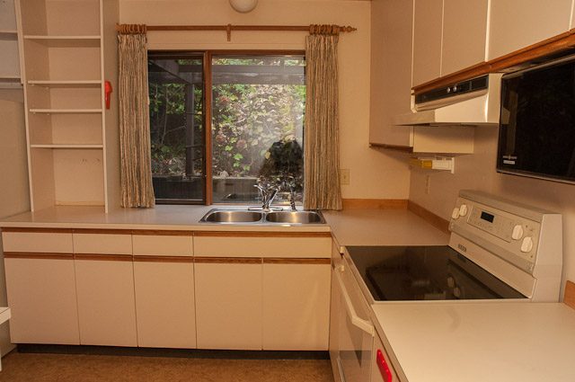 Bright kitchen with light wood cabinets, granite countertops, and a sliding glass door leading to a garden. - 2919 Mathers Ave, West Vancouver