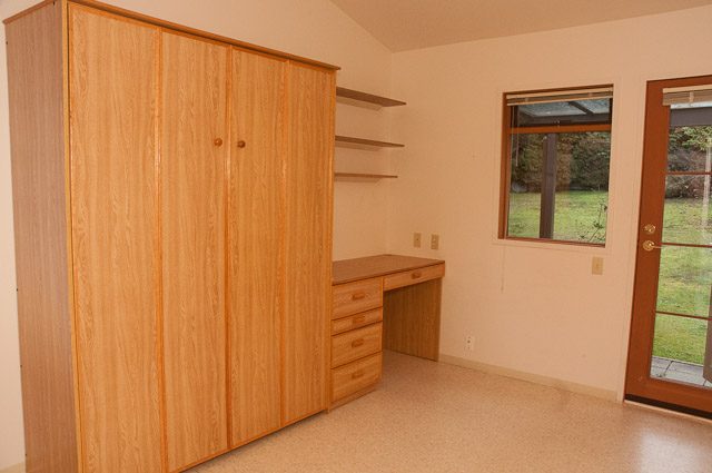 Bright bedroom with wooden wardrobe and built-in desk, city view through window. - 2919 Mathers Ave, West Vancouver