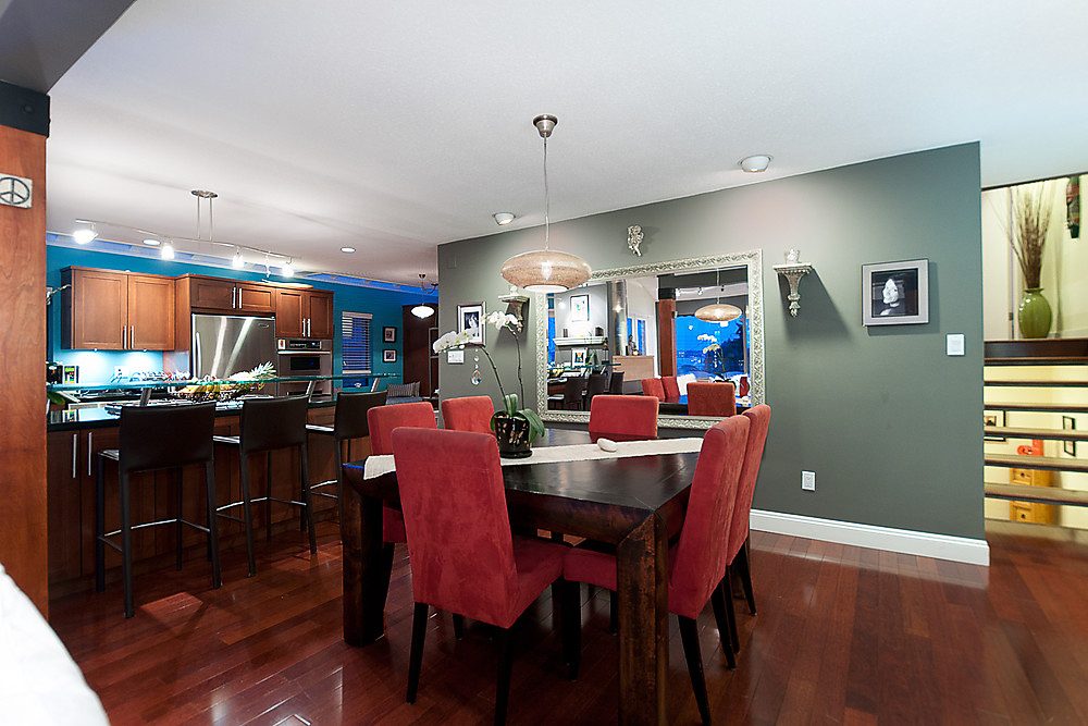 Furnished dining area with red chairs, dark wood table, hardwood floors, and a kitchen in the background. - 1119 Keith Road, West Vancouver