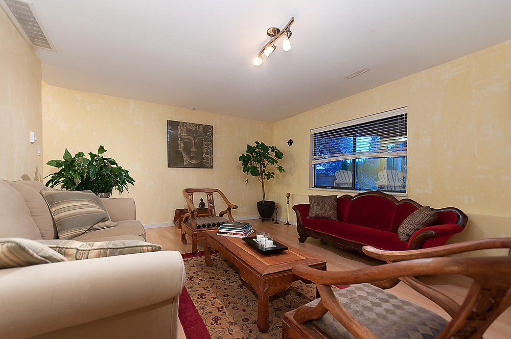 Spacious living room with beige sofas, red accent chair, wooden coffee table, and Buddha wall art. - 1119 Keith Road, West Vancouver