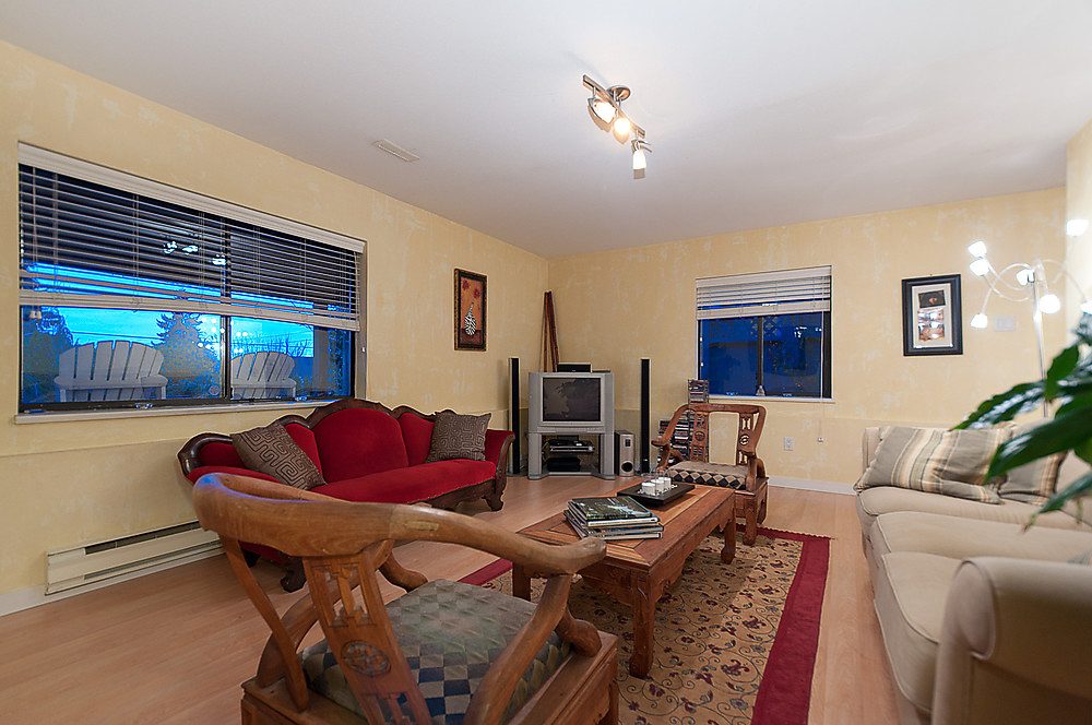 Furnished living room with hardwood floors, red and neutral furniture, and a city view through the windows. - 1119 Keith Road, West Vancouver