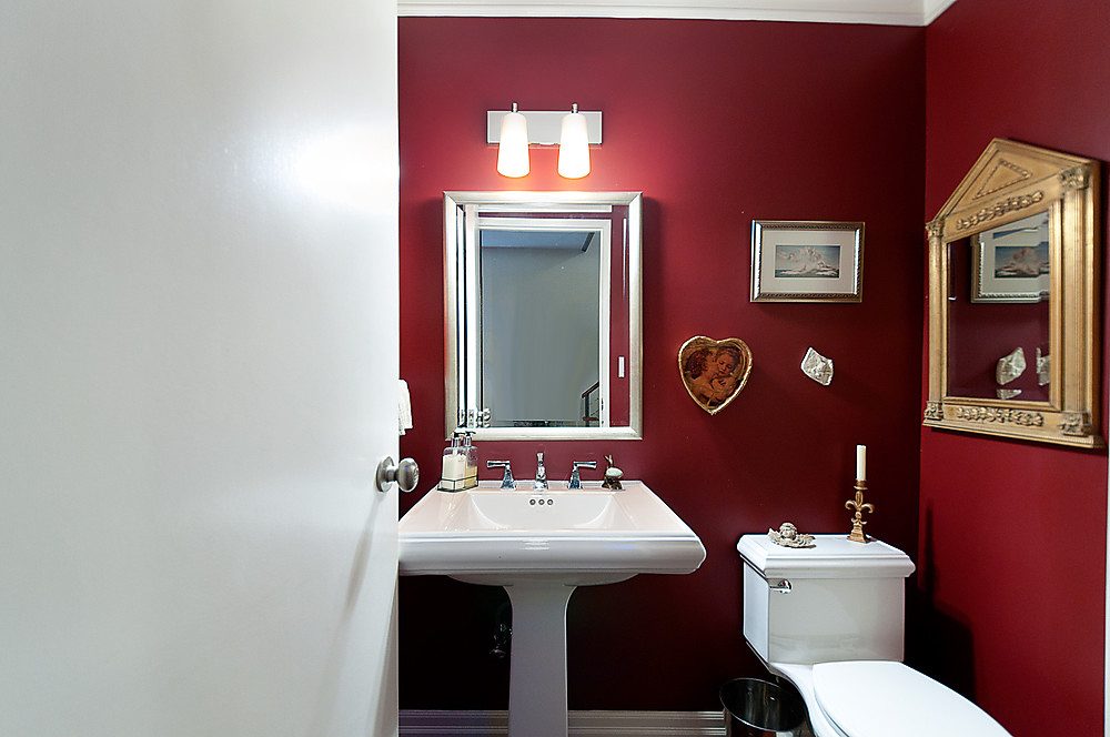 Bathroom with red walls, white sink, gold mirror, and framed artwork. - 1119 Keith Road, West Vancouver