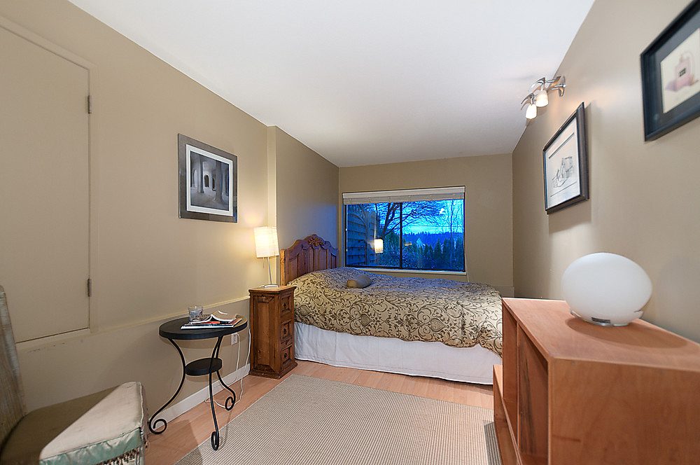 Furnished bedroom with wooden furniture, patterned bedding, and a nightstand with a lamp. - 1119 Keith Road, West Vancouver